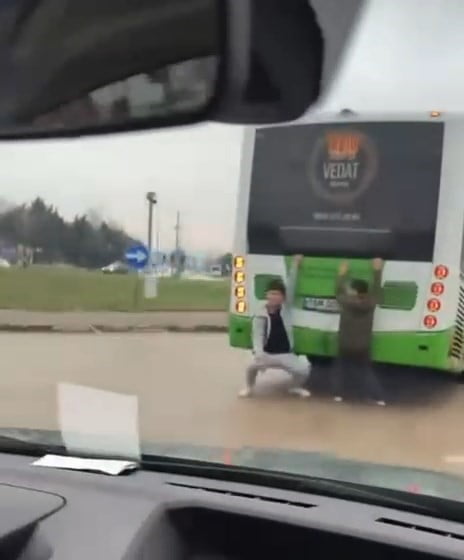 BURSA'DA OTOBÜSÜN ARKASINA TUTUNARAK AYAKLARINI YERE SÜRÜYEN 10-15 YAŞLARINDAKİ 2 ÇOCUK, TRAFİKTE...