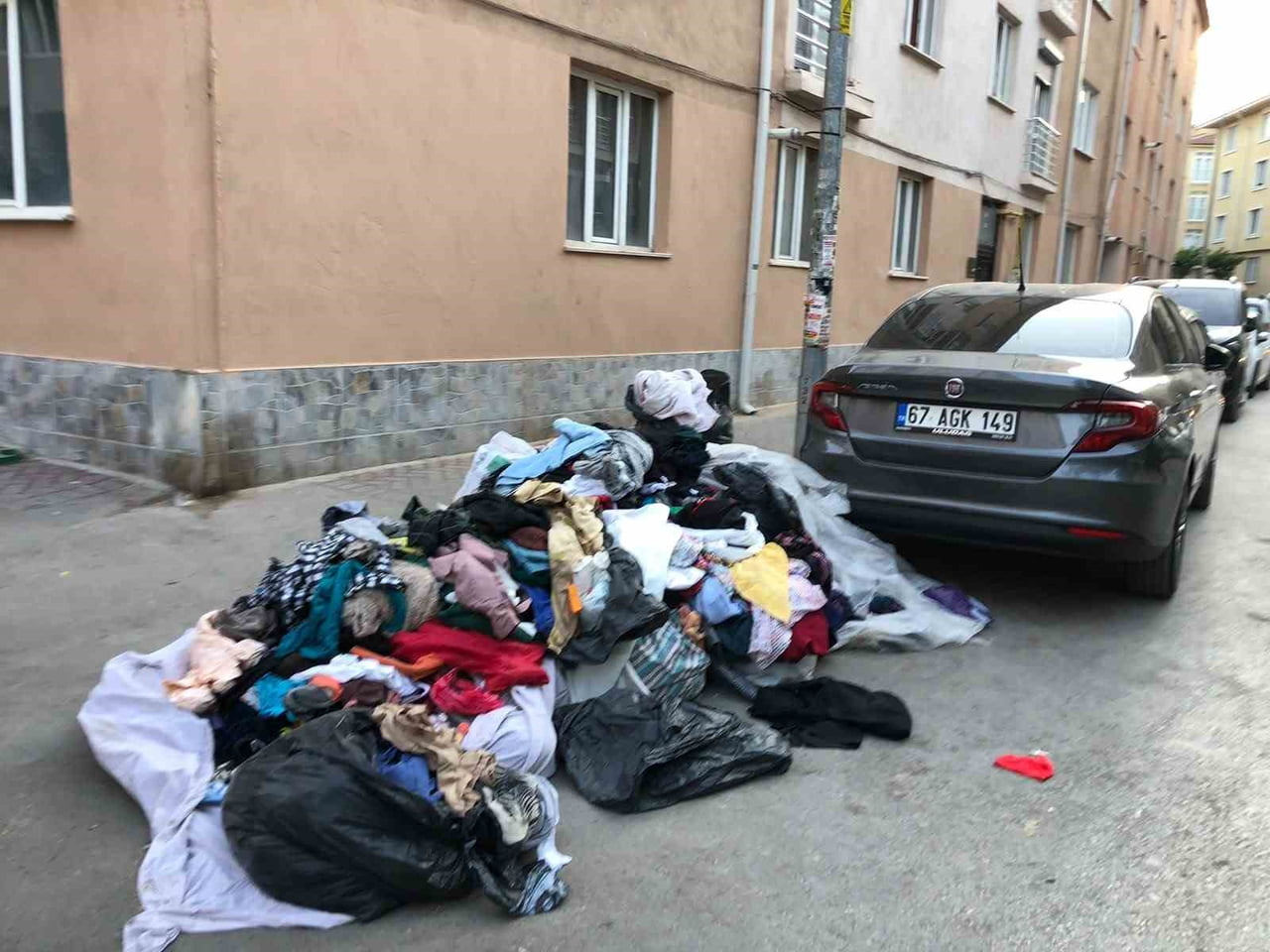 ESKİŞEHİR'İN BİR CADDE ÜZERİNDE ÇÖP KONTEYNERİNİN YANINA BIRAKILAN KIYAFET YIĞINI, HEM YAYA...